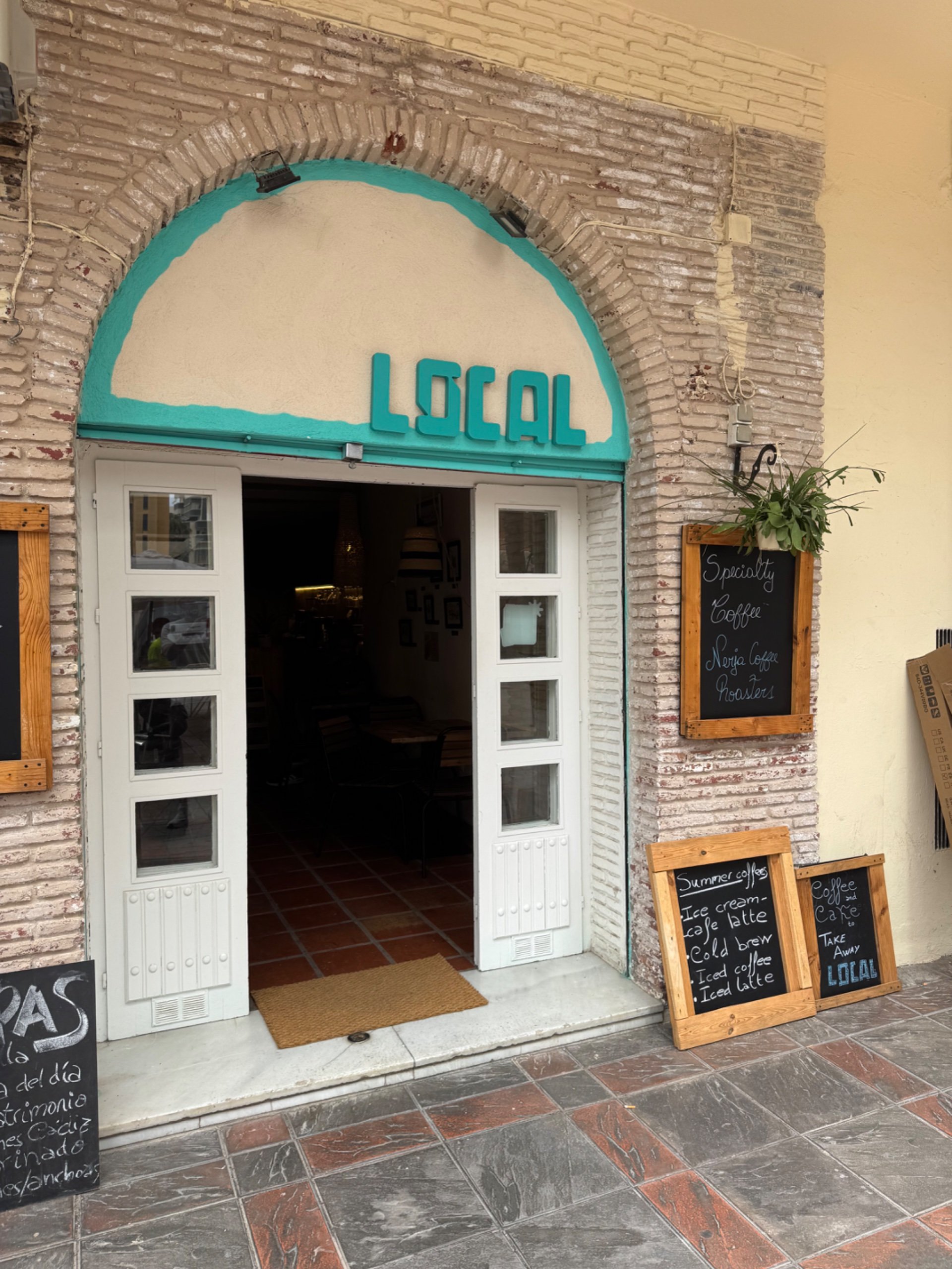 Cihlový vchod s nápisem LOCAL a tabulí „Specialty coffee“